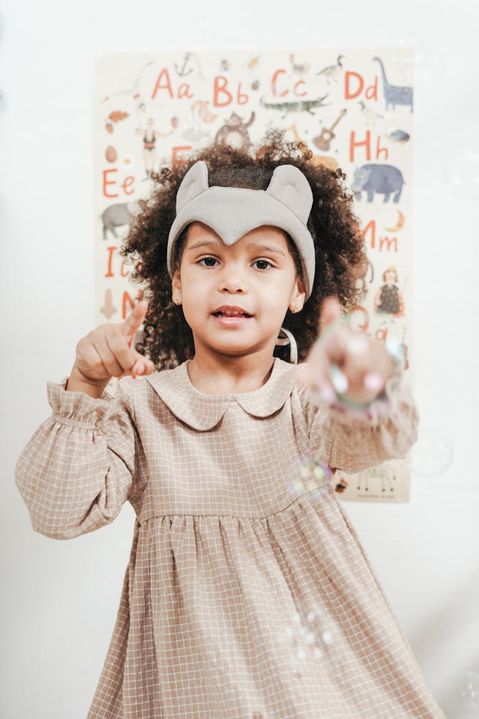 Adorable child in a cute dress playing with bubbles against an alphabet poster.
